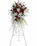 A large floral arrangement on a metal easel stand, featuring red roses, white lilies, and green foliage against a plain white background.
