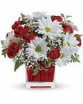 Bouquet of red and white flowers in a clear vase with a red base 