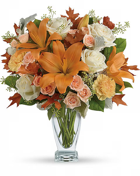 Bouquet of flowers with orange lilies, white and pink roses, and green leaves in a clear vase 