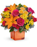 Colorful flower arrangement with orange lilies and pink roses in an orange cube vase